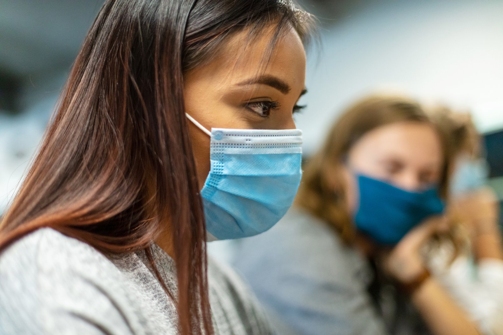 Three female college students wearing face masks using technology working in computer lab.