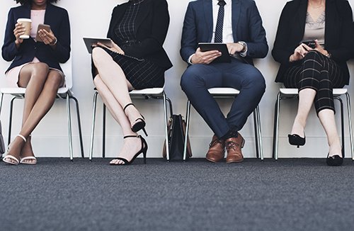 Photo of people dressed in business professional clothing sitting in a line of chairs
