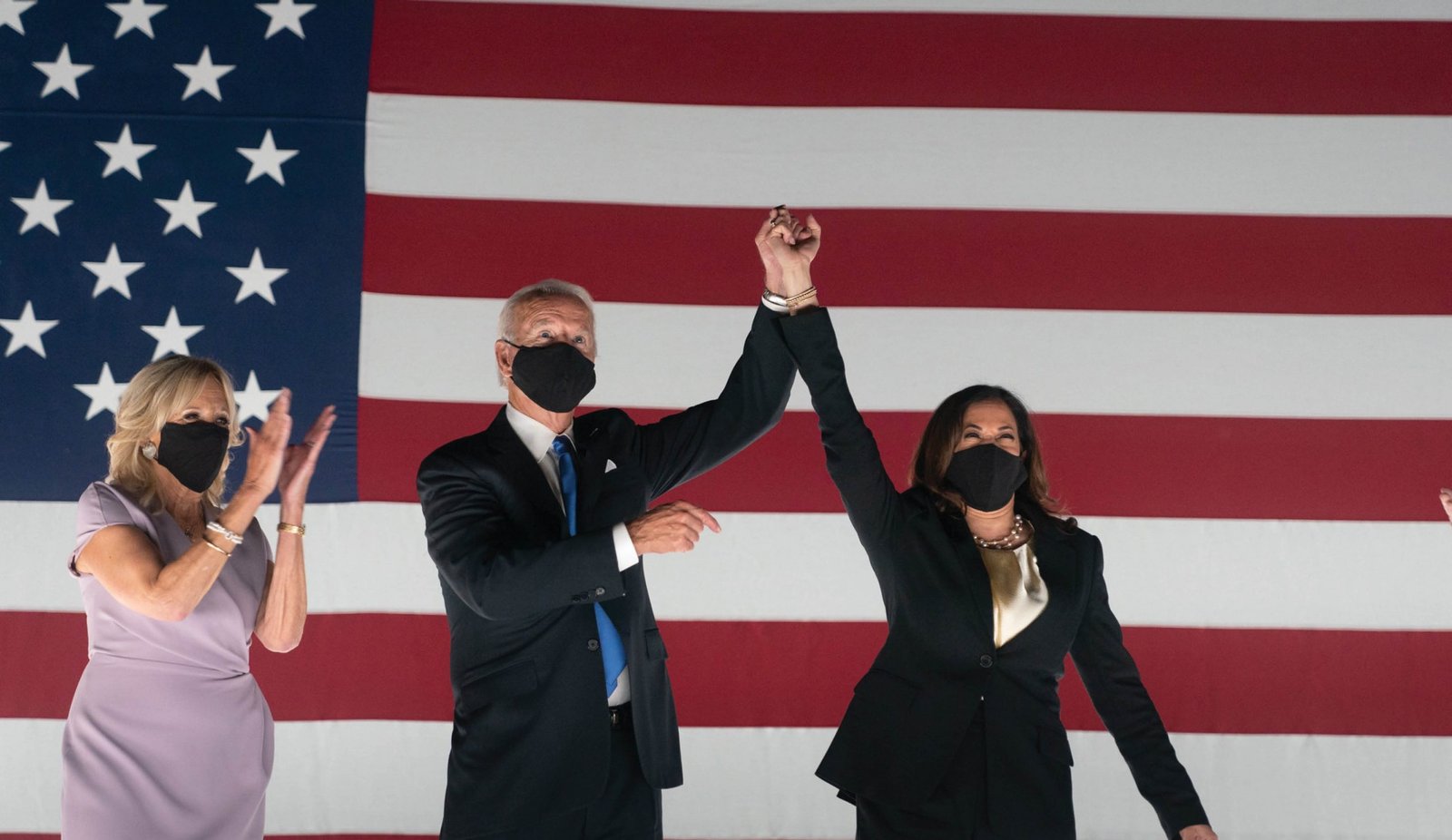 President Joe Biden, Vice President Kamala Harris, and First Lady Jill Biden celebrate their presidential win in front of an American flag.