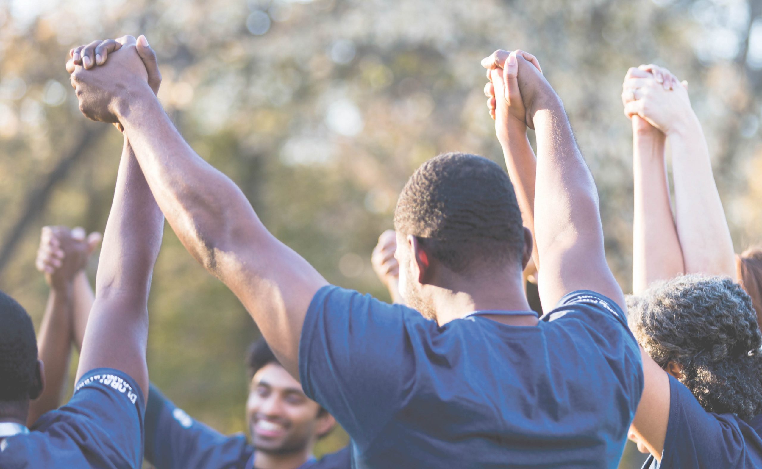 Photo of a group of young Black people holding their hands together in the air.