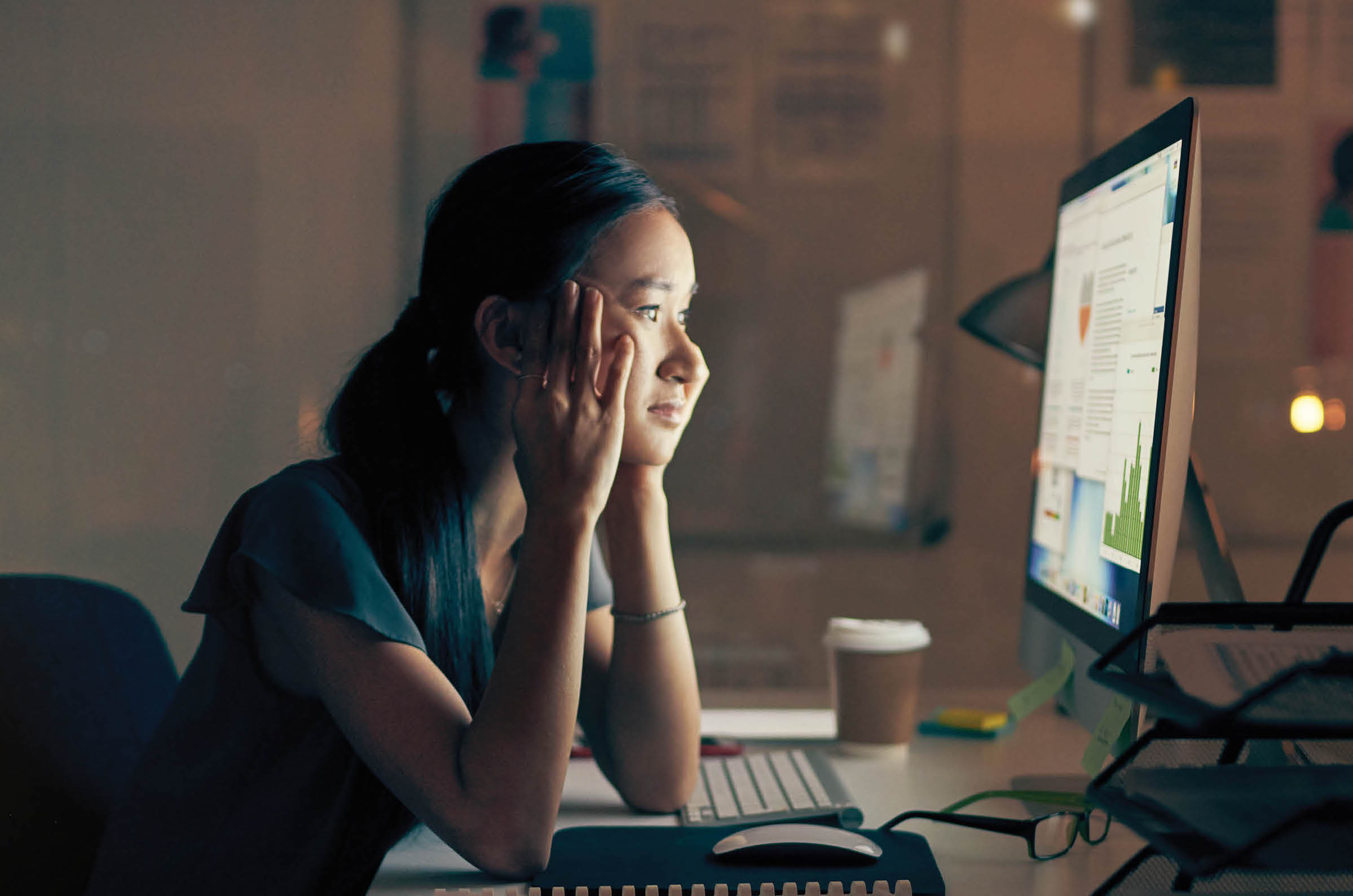 Photo showing a woman sitting at a desk in front of a computer making a concerned face.