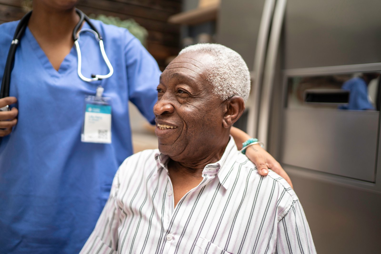 Photo of an older Black man receiving healthcare services from a Black nurse.
