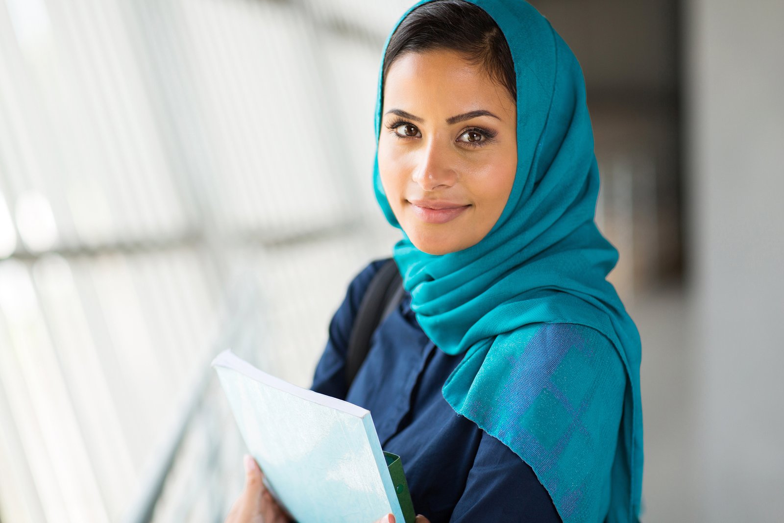 Islamic college student holds a book while looking into camera