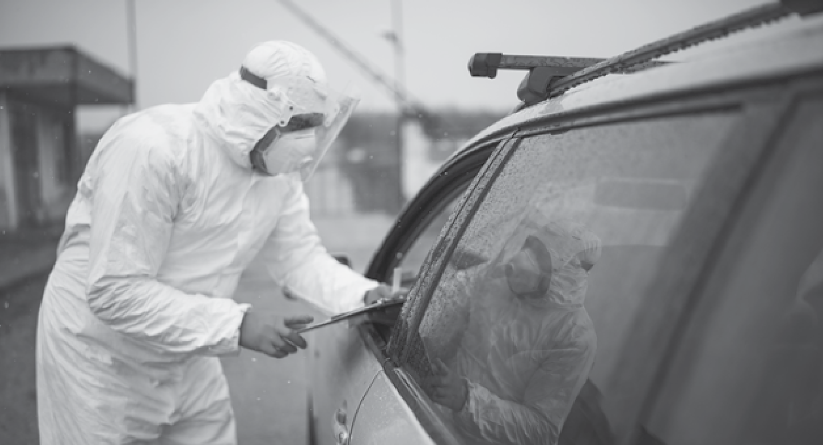 Photo of a man wearing personal protective equipment while standing next to a vehicle with the window rolled down.