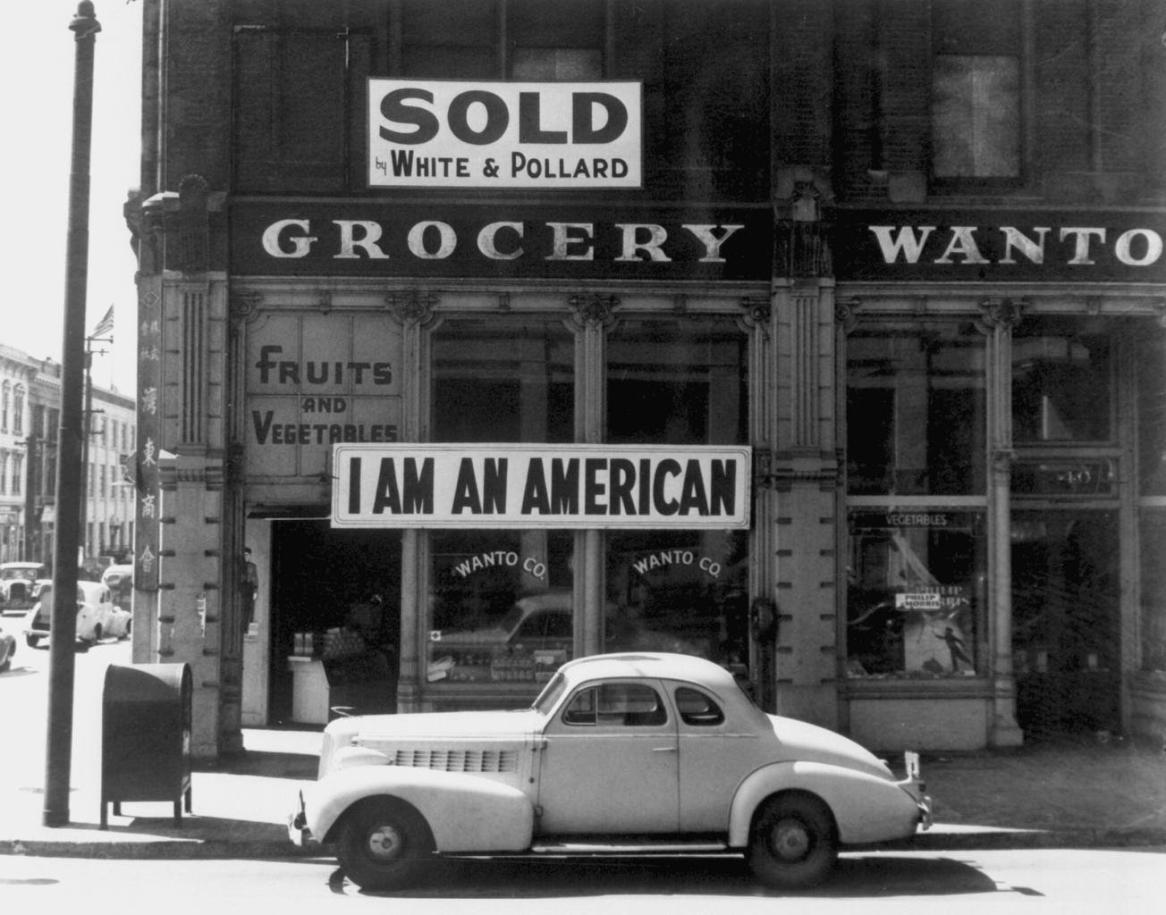 Black and white photo of a storefront with a sign that reads "I am an American"