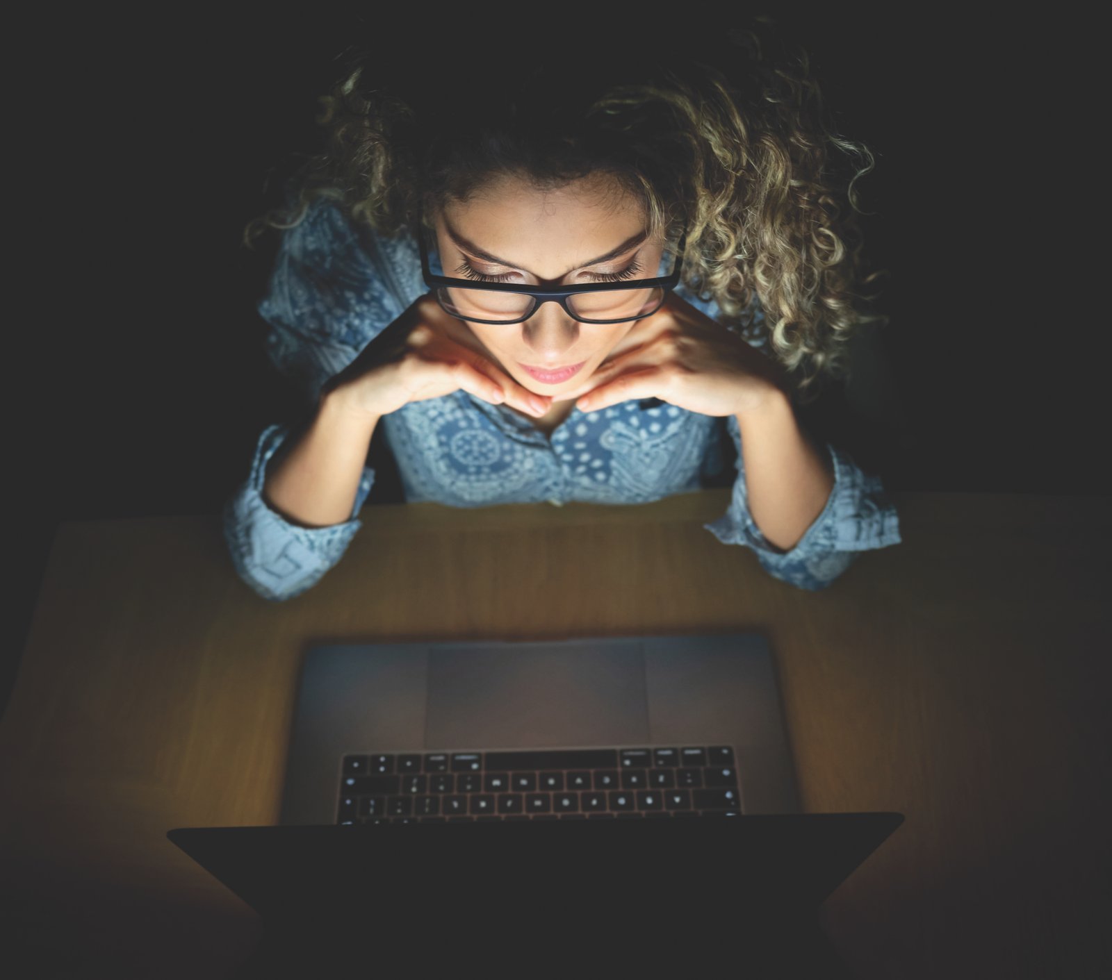 Portrait of a woman at home working at nighttime using a laptop computer and wearing glasses - lifestyle concepts
