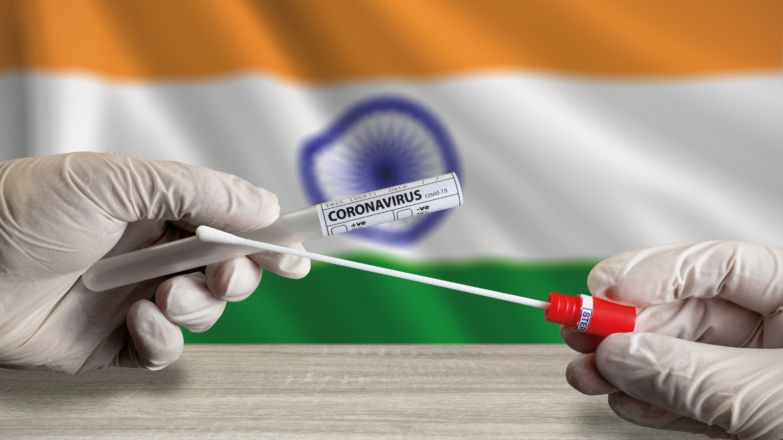 Photo of gloved hands holding a COVID-19 test in front of an Indian flag.