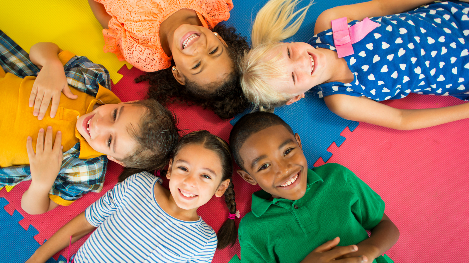 Photo of five diverse children lying on a puzzle mat.