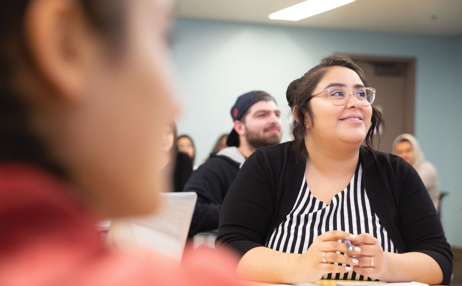 woman sits in a classroom with a person's profile in the foreground