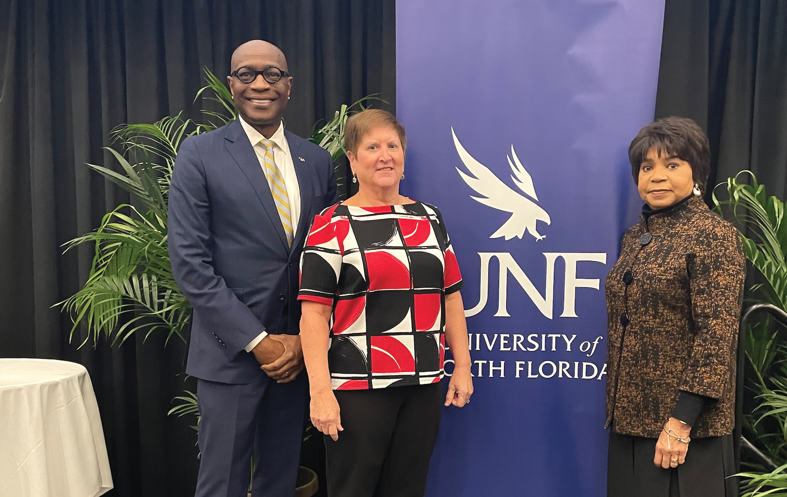 three people pose in front of a UNF banner
