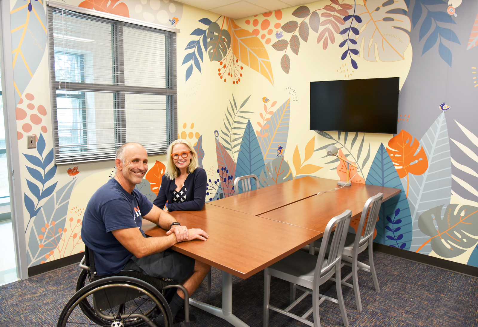 Two people in wheelchairs sit at a conference table
