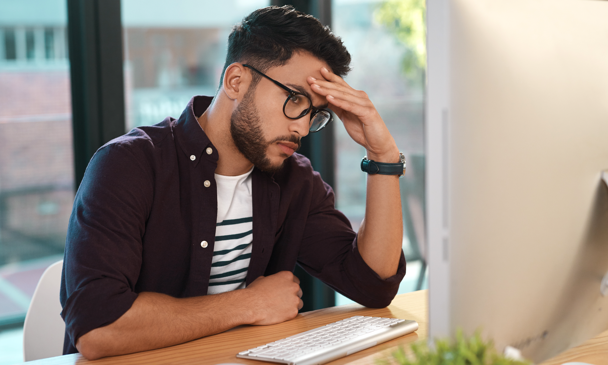Man sitting in front of computer rests his head on his hand